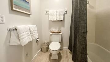 Une petite salle de bain propre, avec des toilettes, deux serviettes blanches posées sur un porte-serviettes, une poubelle et un rideau de douche.