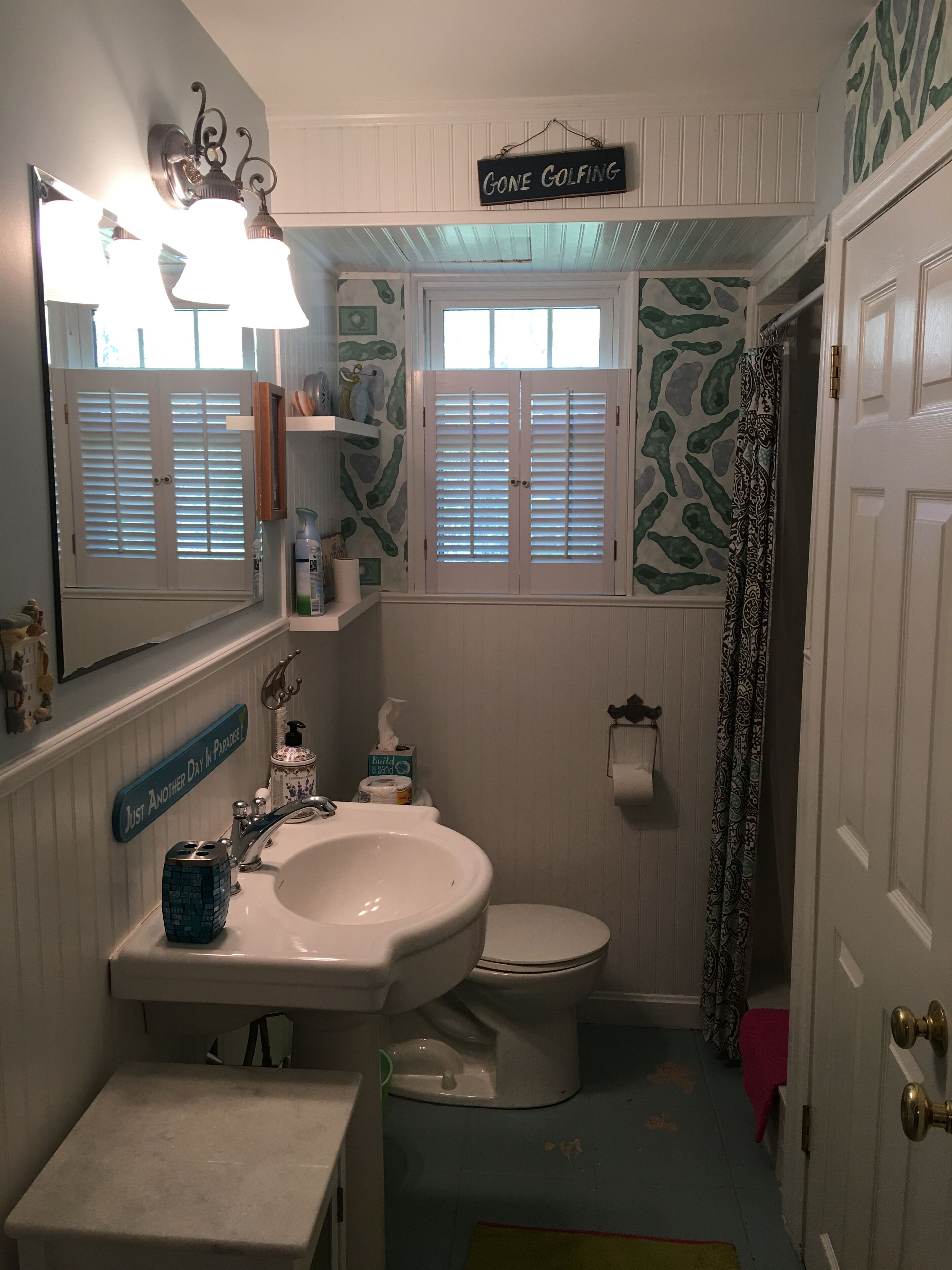 A bathroom with a sink, toilet, and a mirror. There is a sign above the mirror that reads "Gone Golfing".