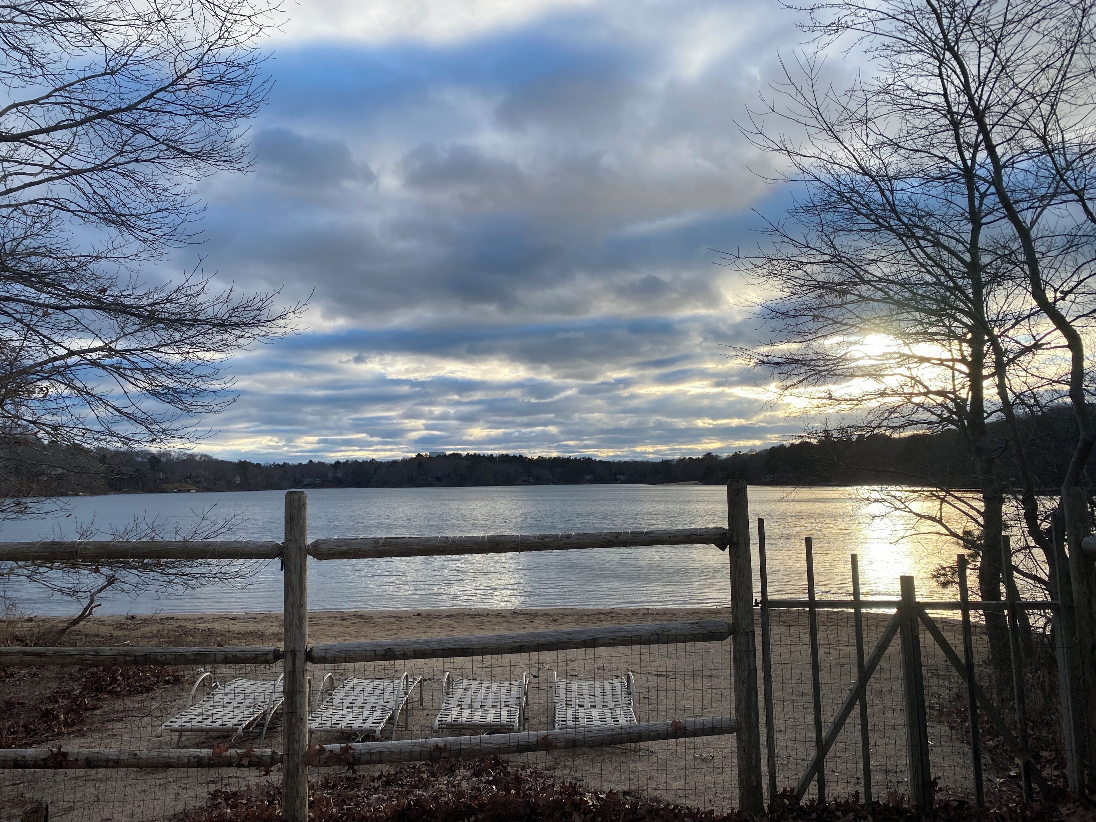 A lakeside view with a wooden fence and metal chairs.
