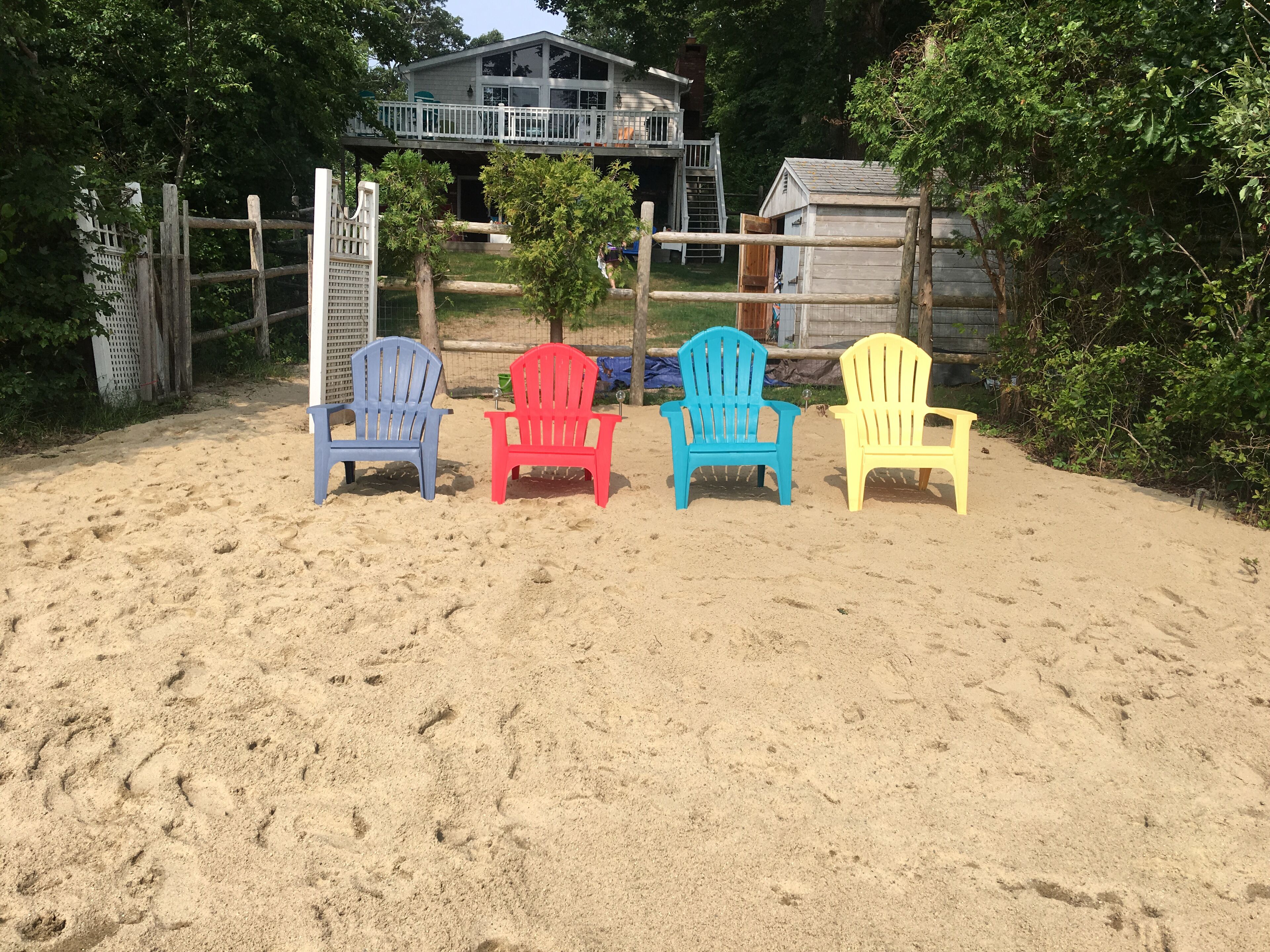 A sandy area with four colorful Adirondack chairs arranged in a row.