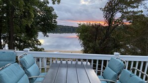 A wooden deck with a table and chairs, overlooking a calm lake and distant shoreline.