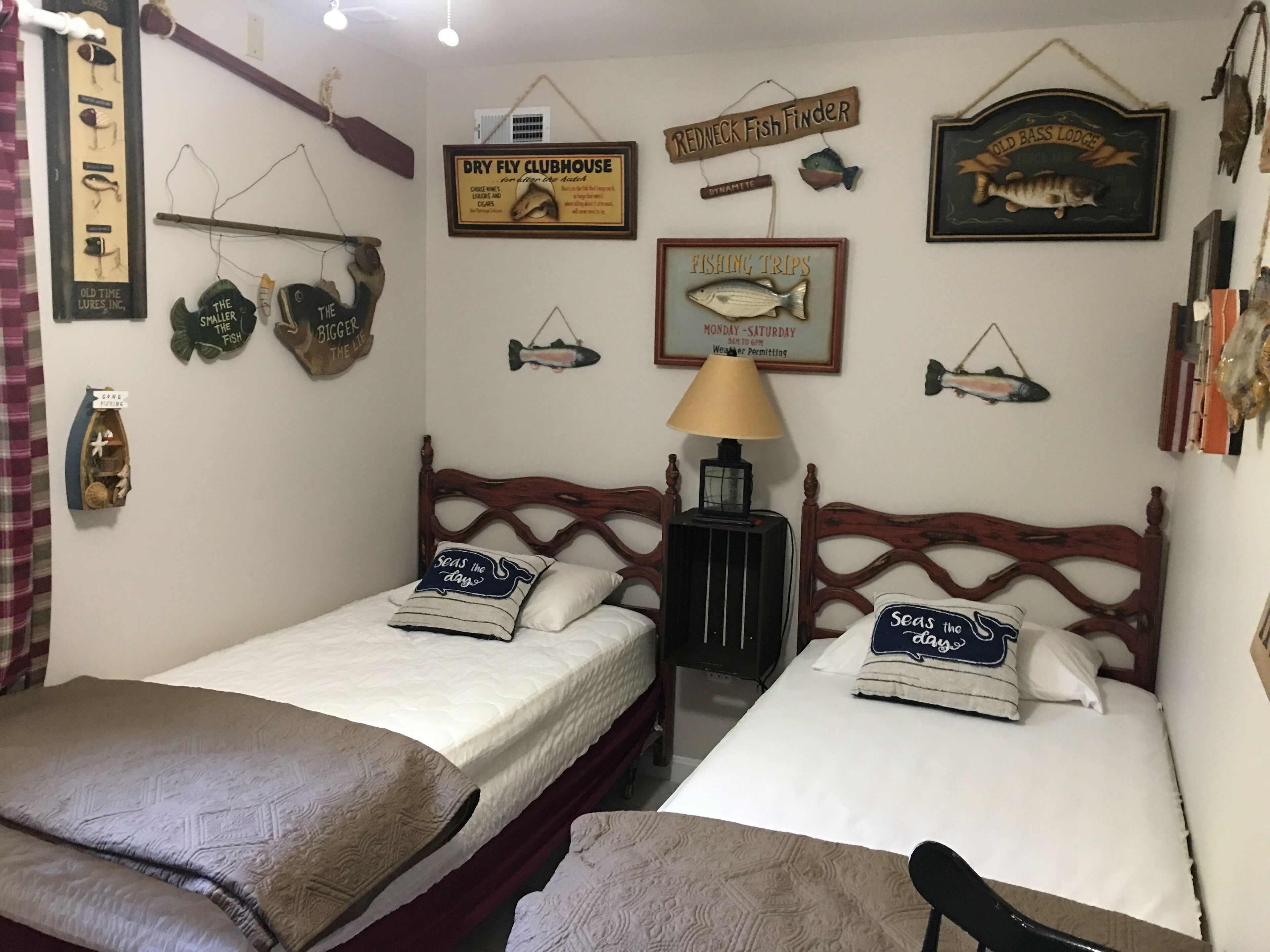 Une pièce avec deux lits en bois, une lampe et divers objets de décoration sur le thème de la pêche accrochés aux murs.