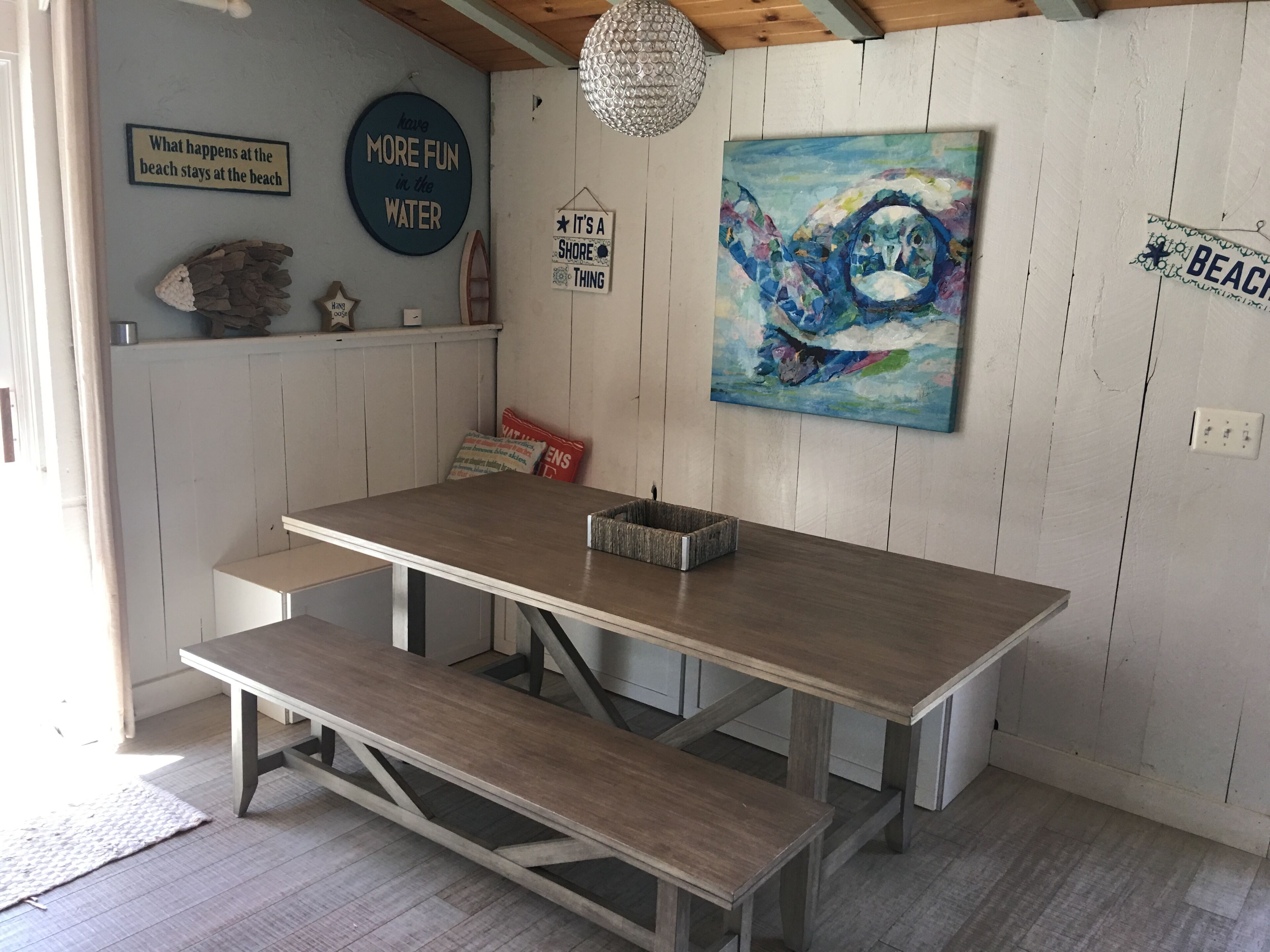 A dining area with a wooden table and benches, a painting on the wall, and various decorative items.