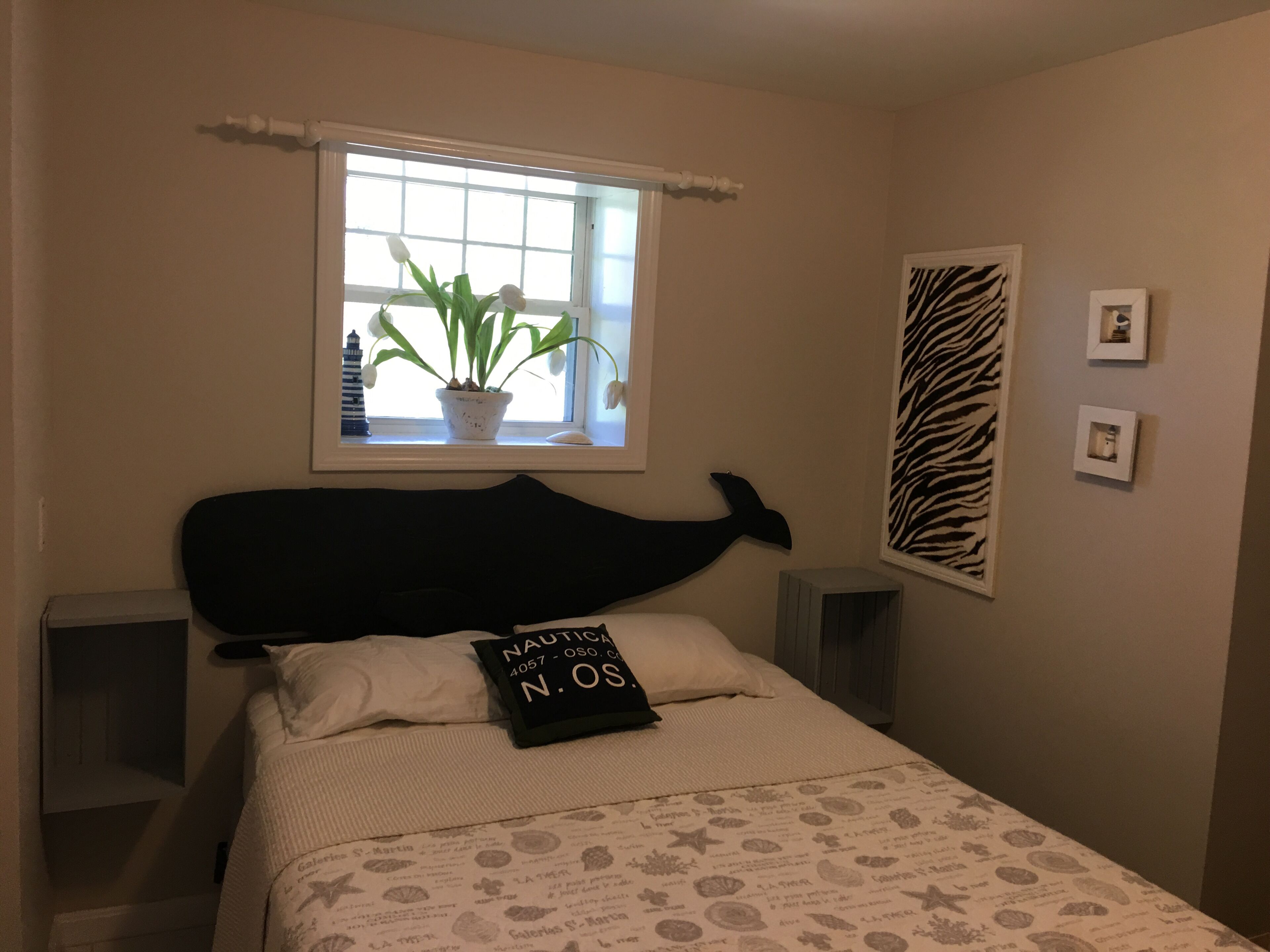 A bedroom with a bed, a window with a plant, a zebra print wall art, and a pillow with text.