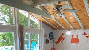 A cozy living room with a blue sofa, a wooden ceiling fan, and a colorful rug.
