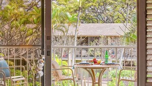 A balcony with a table, chairs, and a view of the surrounding garden and trees. - Beautiful Condo w AC Steps to Napili Bay-Napili Shores E240 (Lahaina)