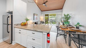 A modern kitchen with white cabinetry, a granite countertop, and a dining area with a wooden table and chairs. - Beautiful Condo w AC Steps to Napili Bay-Napili Shores E240 (Lahaina)