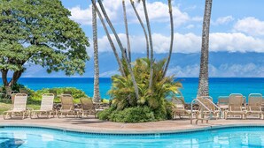 A pool with lounge chairs and palm trees, overlooking a clear blue ocean. - Beautiful Condo w AC Steps to Napili Bay-Napili Shores E240 (Lahaina)