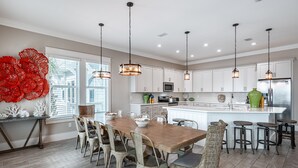 A modern kitchen with white cabinets, a wooden dining table, and hanging pendant lights.