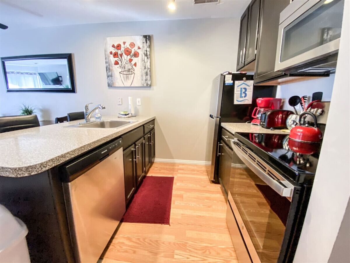 A compact kitchen with a granite countertop, stainless steel appliances, and a red kettle.