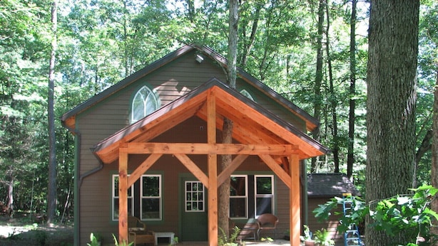 A cabin with a wooden porch, a chimney, and a window.