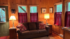 A cozy cabin interior with a brown sofa, two lamps, and framed pictures on the walls.
