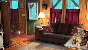 A cozy cabin interior with a wooden interior, a green door, a sofa, a lamp, and a table with a map.