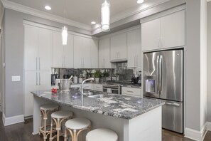 Una cucina moderna con mobili grigi, un frigorifero in acciaio inossidabile, un piano di lavoro in granito e tre sgabelli da bar.