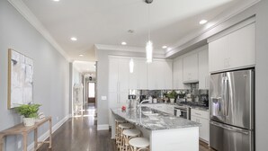 A modern kitchen with white cabinets, a stainless steel refrigerator, and a marble countertop.