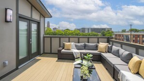 A rooftop terrace with a sectional sofa, a small table with a plant, and a city view.
