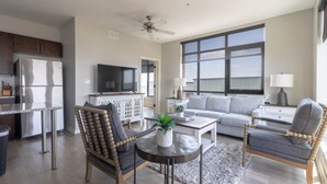 A modern living room with a grey sofa, two wooden chairs, a coffee table, and a TV.