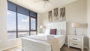 A bedroom with a large window, a bed, a nightstand, and a ceiling fan.