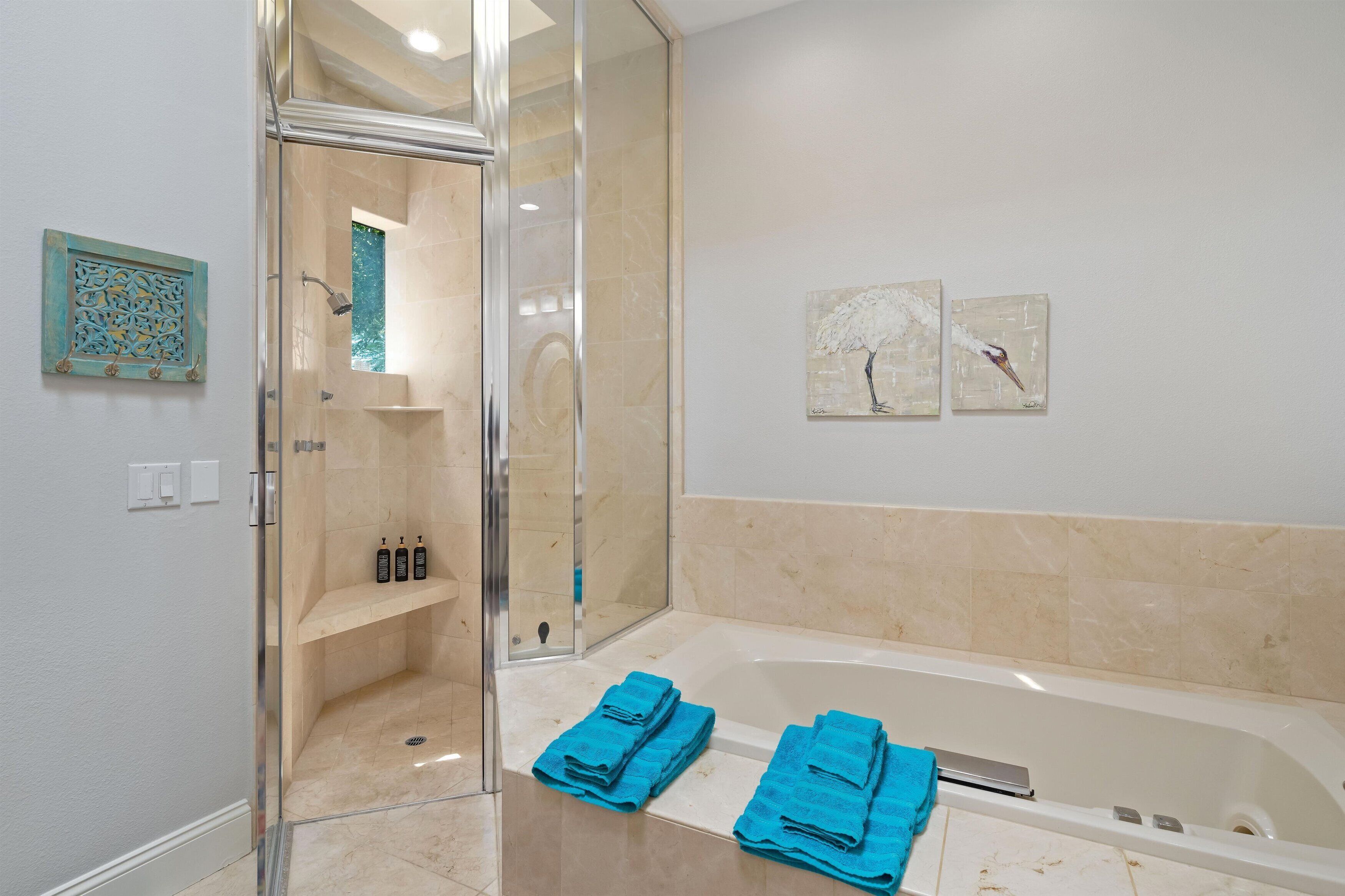 Un baño moderno con ducha de vidrio, bañera y dos obras de arte colgantes.