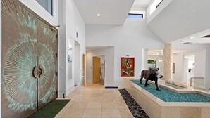 A spacious lobby with a large decorative door, a glass fish tank with a sculpture, and a colorful painting on the wall. - Newly Remodeled 4,400 Square Foot Modern design with Pool and Spa. #065893 (La Quinta)