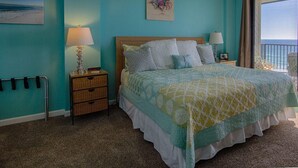 Quarto com cama, mesas de cabeceira, luminária, pintura e vista para o oceano.