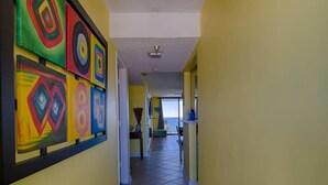 Um corredor com arte abstrata geométrica nas paredes, que dá para um quarto com vista do céu.