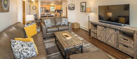 A living room with a sofa, coffee table, TV, and kitchen in the background.