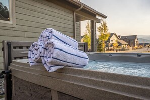 A hot tub with towels stacked on its edge, set against a backdrop of a wooden house and a clear sky.