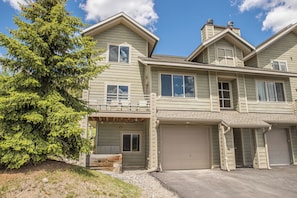 A two-story house with a garage, a covered porch, and a large evergreen tree.