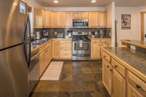 A modern kitchen with wooden cabinets, stainless steel appliances, granite countertops, and a tiled floor. - Condo w/private hot tub close to Big Sky Resort & Town Center | Comfort Awaits At Deer Run (Gallatin Gateway)