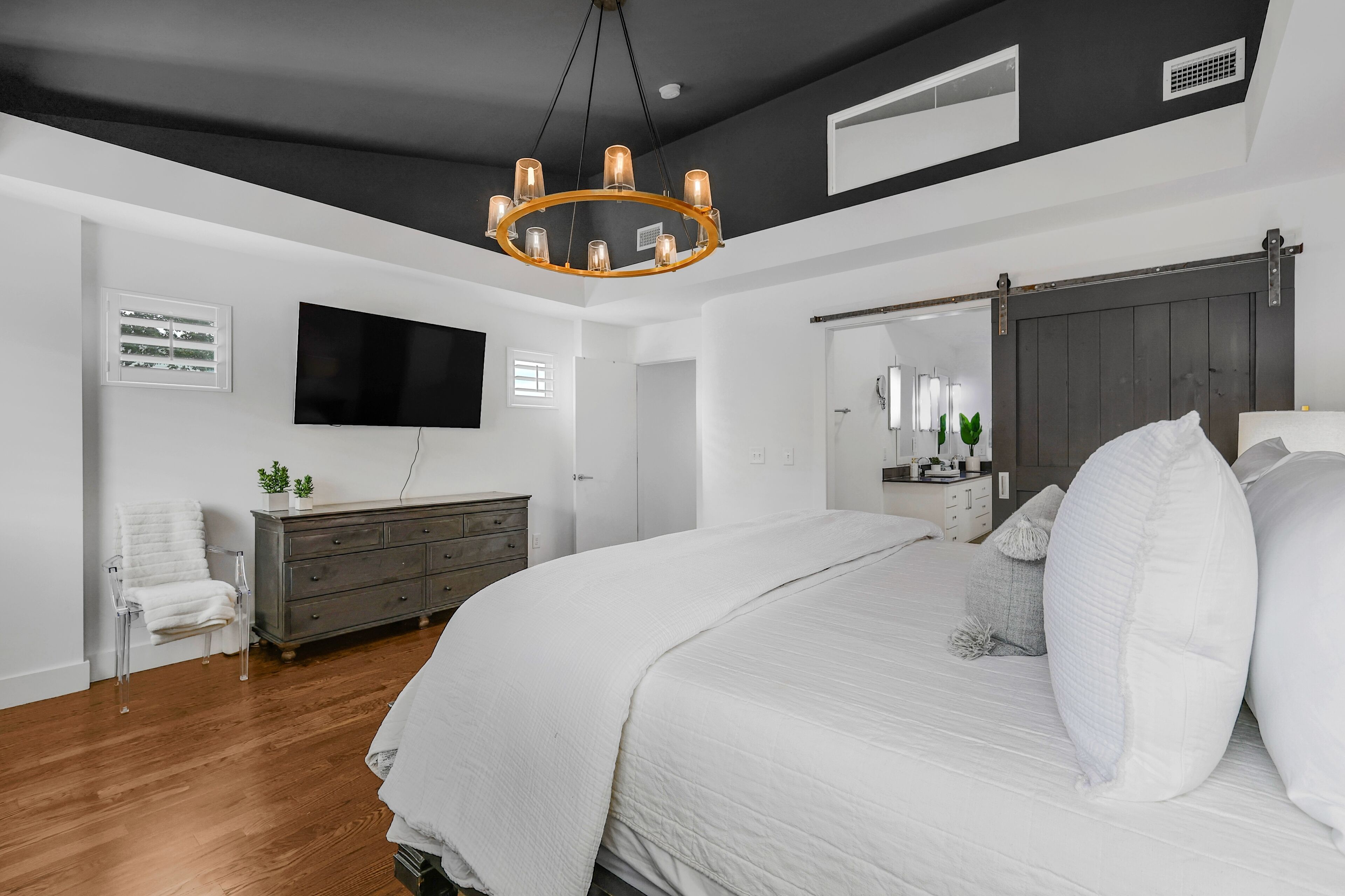 A bedroom with a large bed, a chandelier, a dresser, a TV, and a sliding door closet.