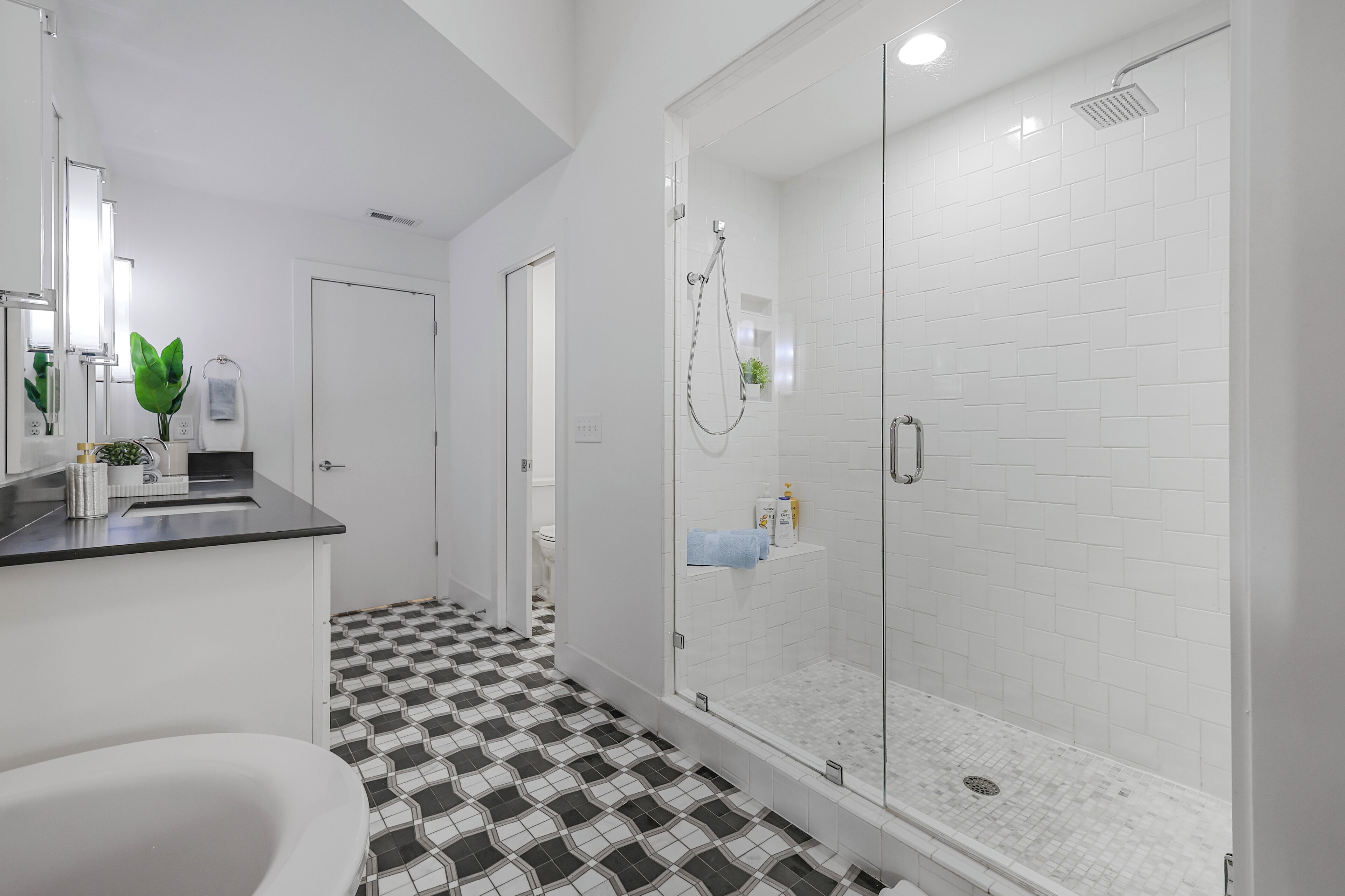 A modern bathroom with a glass-enclosed shower, a black and white checkered floor, and a white sink with a mirror.