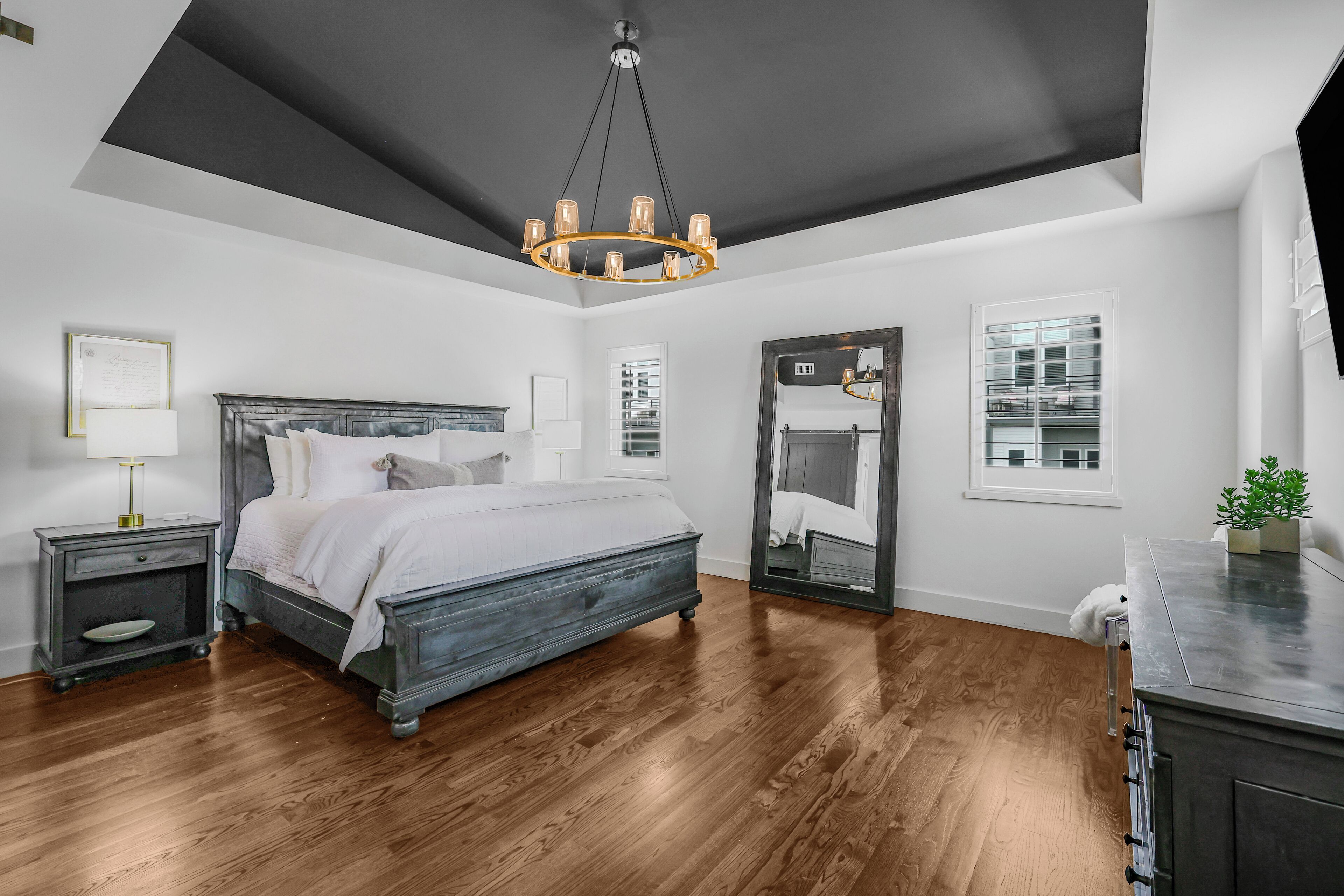 A bedroom with a bed, bedside tables, a mirror, and a chandelier.