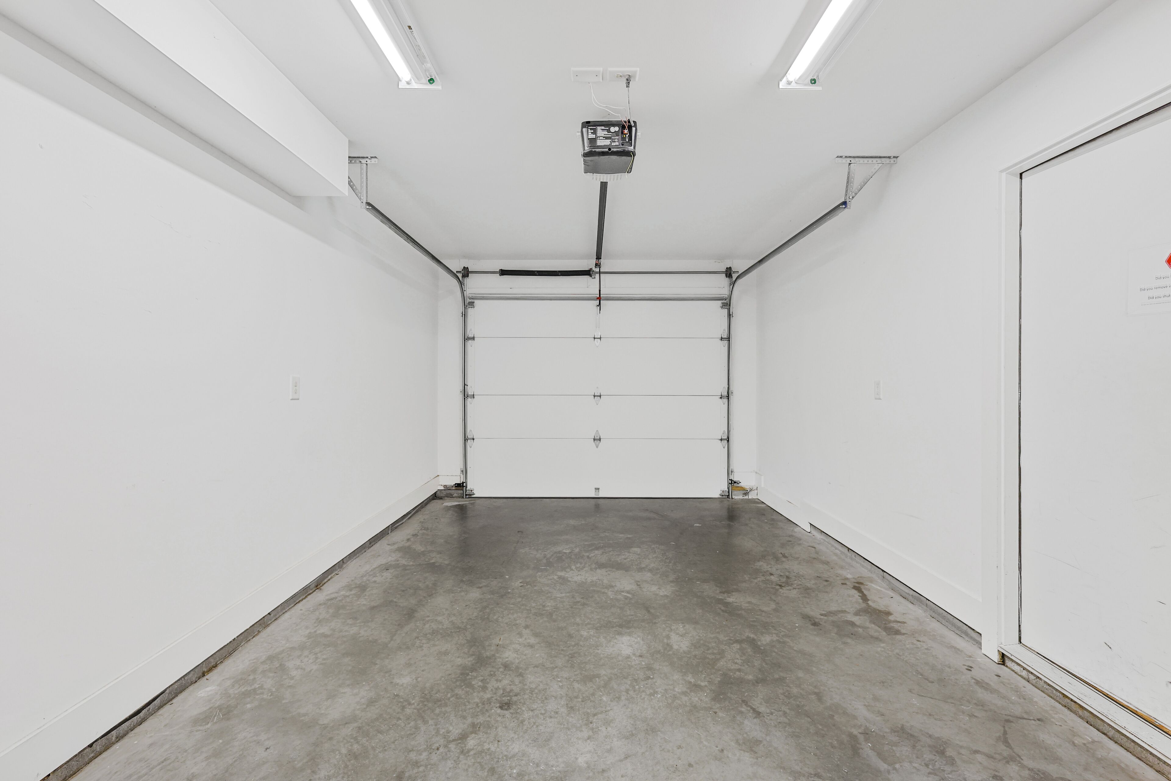 Une pièce propre et vide, avec des murs blancs, un sol en béton et une porte fermée.