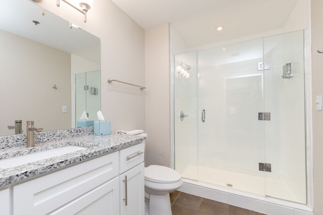 Une salle de bain moderne avec un comptoir en granit, des toilettes blanches et une douche à parois de verre.