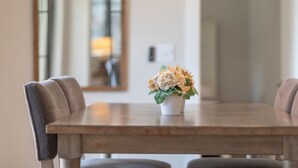 Una mesa de comedor con un centro de mesa floral, dos sillas tapizadas y un espejo en la pared.
