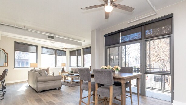 Un salón espacioso con zona de comedor, ventanas grandes y ventilador de techo.