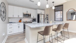 Una cocina moderna con armarios blancos, encimera de granito, electrodomésticos de acero inoxidable y una zona de bar con taburetes.