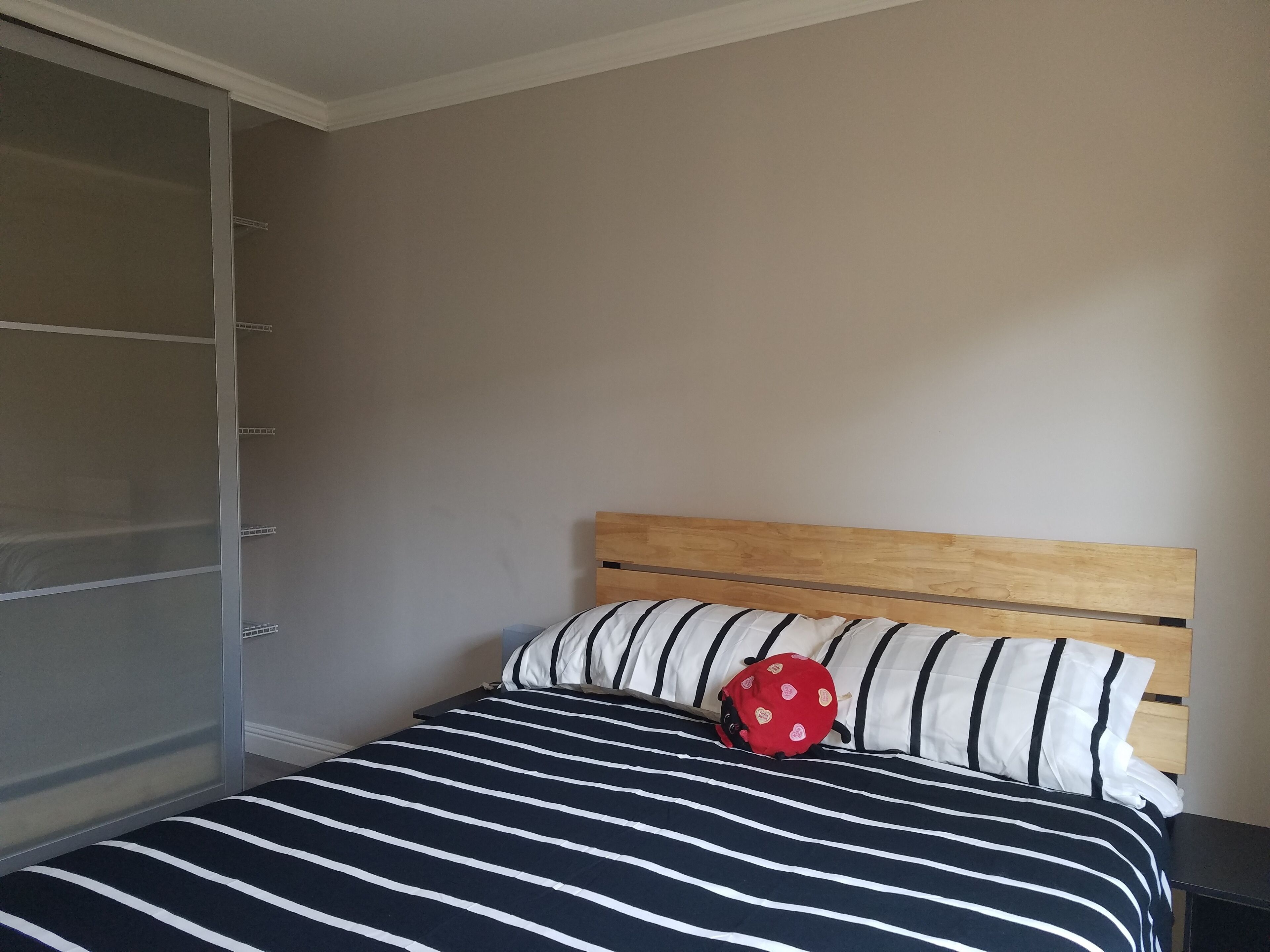 Un dormitorio con una cama, cabecera de madera, colcha a rayas y almohada con forma de mariquita roja.