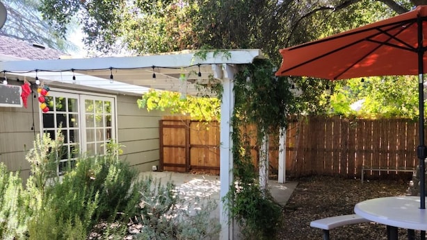 A patio area with a white pergola, a wooden fence, and a table with benches. - 3 bed 2 bath home in heart of Silicon Valley (Redwood City)