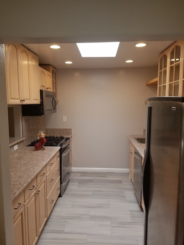 A kitchen with beige cabinets, a stainless steel refrigerator, a microwave, and a gas stove.