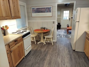 A kitchen with wooden cabinets, a stove, a dining table with chairs, and a refrigerator.