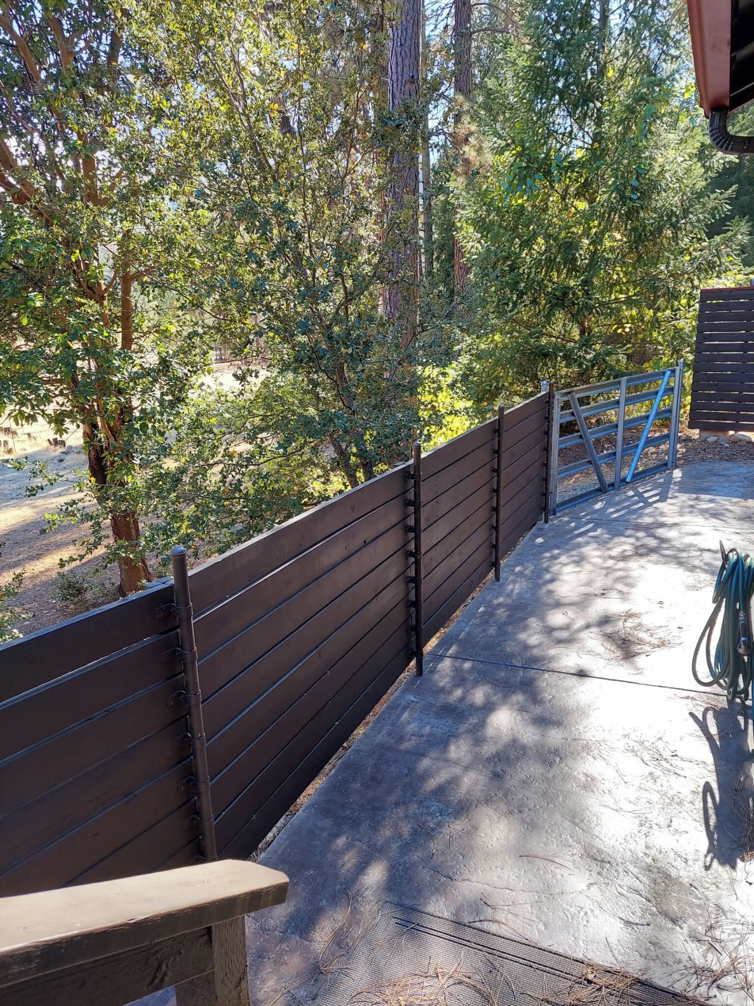 A concrete pathway leading to a wooden fence with a metal gate, surrounded by trees.