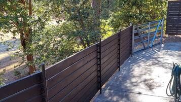 A concrete pathway leading to a wooden fence with a metal gate, surrounded by trees.