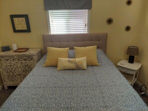 Une chambre à coucher comprenant un lit, des tables de chevet, une commode, une fenêtre avec des stores et des éléments de décoration murale.