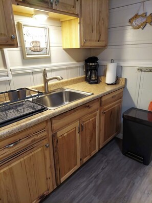 Una cocina con armarios de madera, un lavamanos de acero inoxidable, una cafetera y un dispensador de toallas de papel.