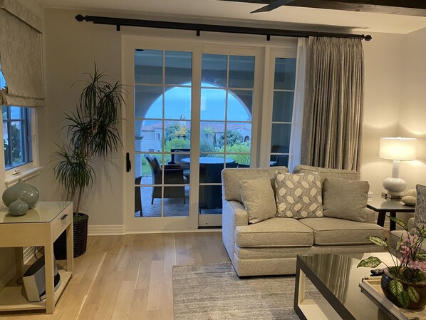 A living room with a sofa, a coffee table, a lamp, and a view through a glass door to an outdoor patio.
