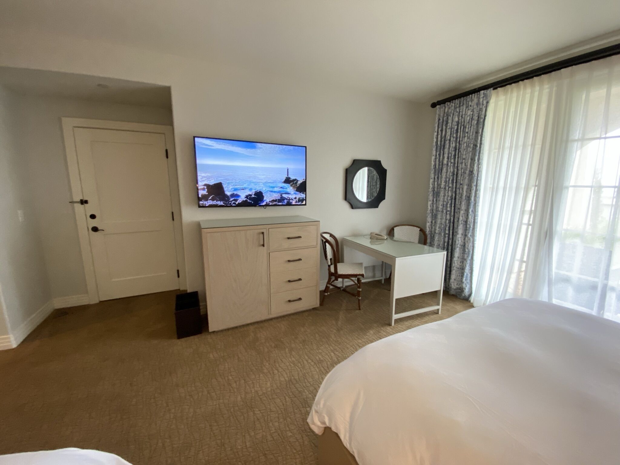 A hotel room with a bed, a desk, a television, a mirror, and a window with curtains.