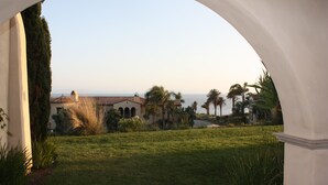 A view through an arched doorway of a building with a lawn and palm trees, overlooking a body of water.