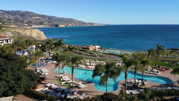 A resort with a large pool area, palm trees, and a view of the ocean.